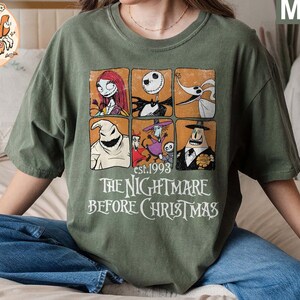May include: A green t-shirt with a vintage-style graphic of characters from the movie "The Nightmare Before Christmas". The graphic includes Jack Skellington, Sally, Oogie Boogie, and Zero. The text "est. 1993" and "The Nightmare Before Christmas" is printed below the graphic.
