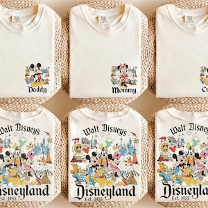 Puede incluir: Camisetas de color crema con gr&aacute;ficos de personajes de Disney. La fila superior presenta camisetas con las etiquetas "Daddy", "Mommy" y "Custom". La fila inferior muestra camisetas con un gr&aacute;fico de Disneyland y el texto "Est. 1955."