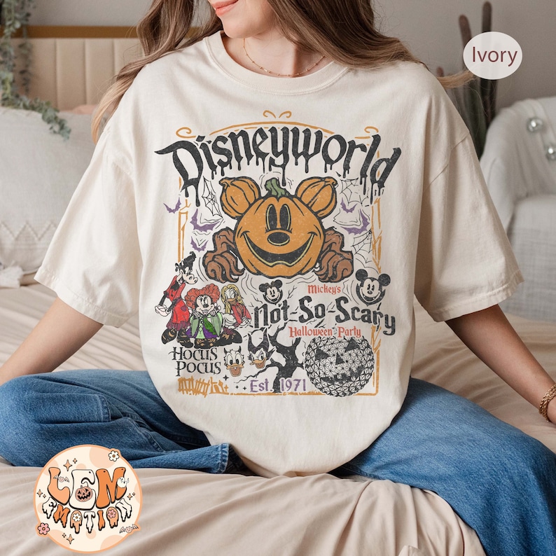Op de afbeelding: Een wit T-shirt met een vintage-stijl afbeelding van Mickey Mouse verkleed als een pompoen. De afbeelding bevat de tekst "Disneyworld", "Mickey's Not-So-Scary Halloween Party", "Hocus Pocus", en "Est. 1971".