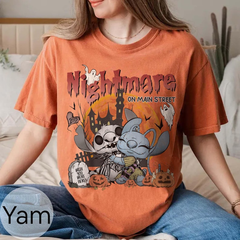 Puede incluir: Camiseta naranja con un dise&ntilde;o de Halloween que dice "Nightmare on Main Street". El dise&ntilde;o incluye personajes de dibujos animados, calabazas, una casa embrujada y fantasmas. La camiseta es de estilo casual.