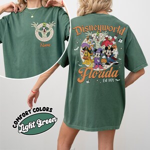 May include: Light green t-shirt with a Disney World Florida graphic. The front features a cartoon character in mummy wrappings. The back displays Disney characters with the text "Disneyworld Florida Est 1971". The shirt is labeled "Comfort Colors Light Green".