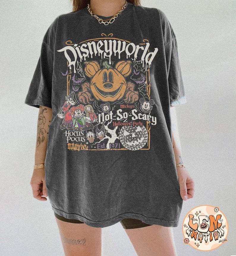 Op de afbeelding: Een zwart T-shirt met een vintage-stijl grafische afbeelding van Mickey Mouse en zijn vrienden die Halloween vieren in Disney World. De afbeelding bevat een pompoen-gekopte Mickey Mouse, een griezelige boom en de tekst "Mickey's Not-So-Scary Halloween Party" en "Est. 1971".