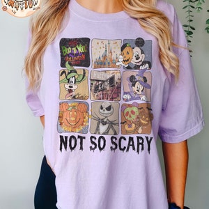 May include: A purple t-shirt with a collage of images featuring Mickey Mouse, Goofy, and Jack Skellington. The images are in a grid pattern and include pumpkins, a castle, and a sign that says "Hollywood." The text "Not So Scary" is printed below the images.