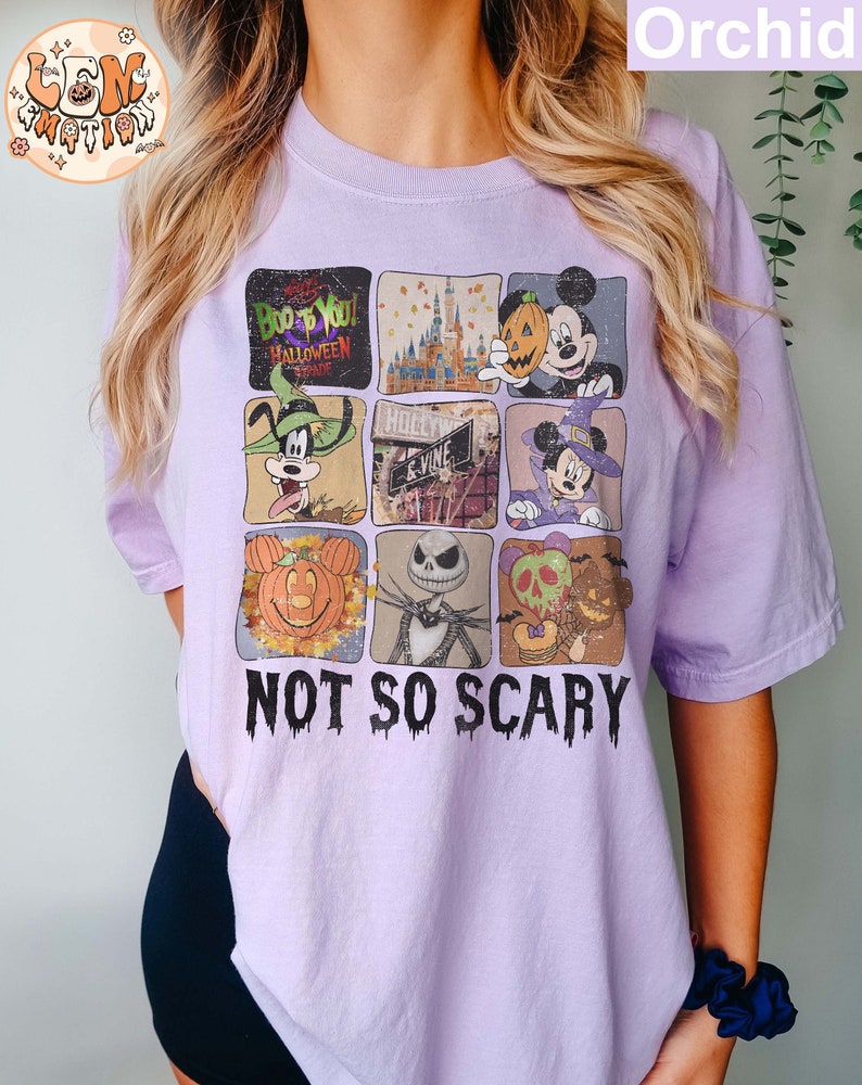 May include: A purple t-shirt with a collage of images featuring Mickey Mouse, Goofy, and Jack Skellington. The images are in a grid pattern and include pumpkins, a castle, and a sign that says "Hollywood." The text "Not So Scary" is printed below the images.