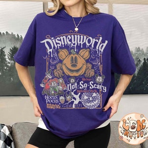 Op de afbeelding: Paars T-shirt met een afbeelding van Mickey Mouse en andere Disney-figuren. De tekst op het shirt luidt "Disneyworld Mickey's Not-So-Scary Halloween Party, Est. 1971".