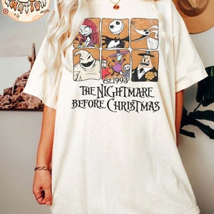May include: A white t-shirt with a vintage-style graphic of characters from the movie "The Nightmare Before Christmas". The graphic features a grid of six squares, each containing a different character from the film. The text "est. 1993" and "The Nightmare Before Christmas" is printed below the graphic.