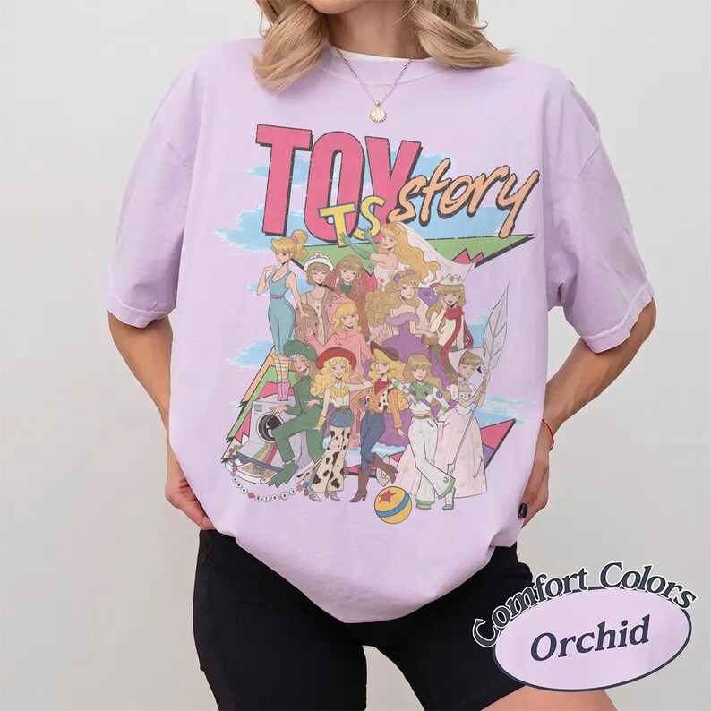 Peut inclure: Un t-shirt &agrave; manches courtes violet clair avec une impression graphique de divers personnages anim&eacute;s et le texte "TOY story". Le motif comprend un arri&egrave;re-plan g&eacute;om&eacute;trique color&eacute;, une balle jaune et bleue, et plusieurs personnages en tenues vari&eacute;es.