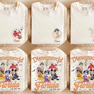 May include: Cream-colored t-shirts with Disney character designs. The shirts feature Donald Duck, Goofy, and Mickey Mouse in Halloween costumes. The bottom shirts have a "Disneyworld Florida Est 1971" graphic.
