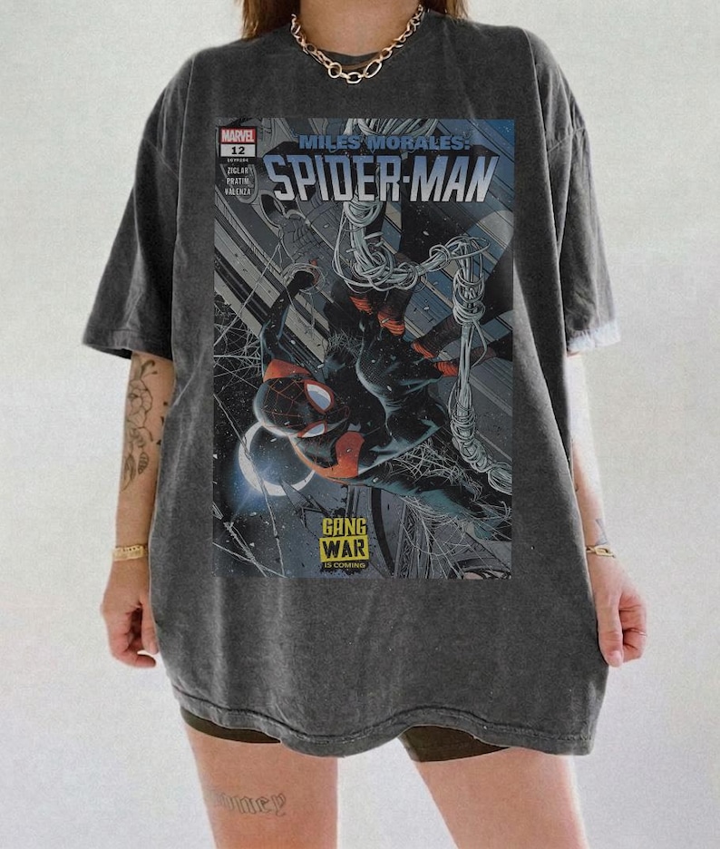 Op de afbeelding: Donkergrijs t-shirt met een Spider-Man stripboekcover. De afbeelding bevat de tekst "Miles Morales: Spider-Man" en "Gang War", met een dynamische illustratie van de superheld.