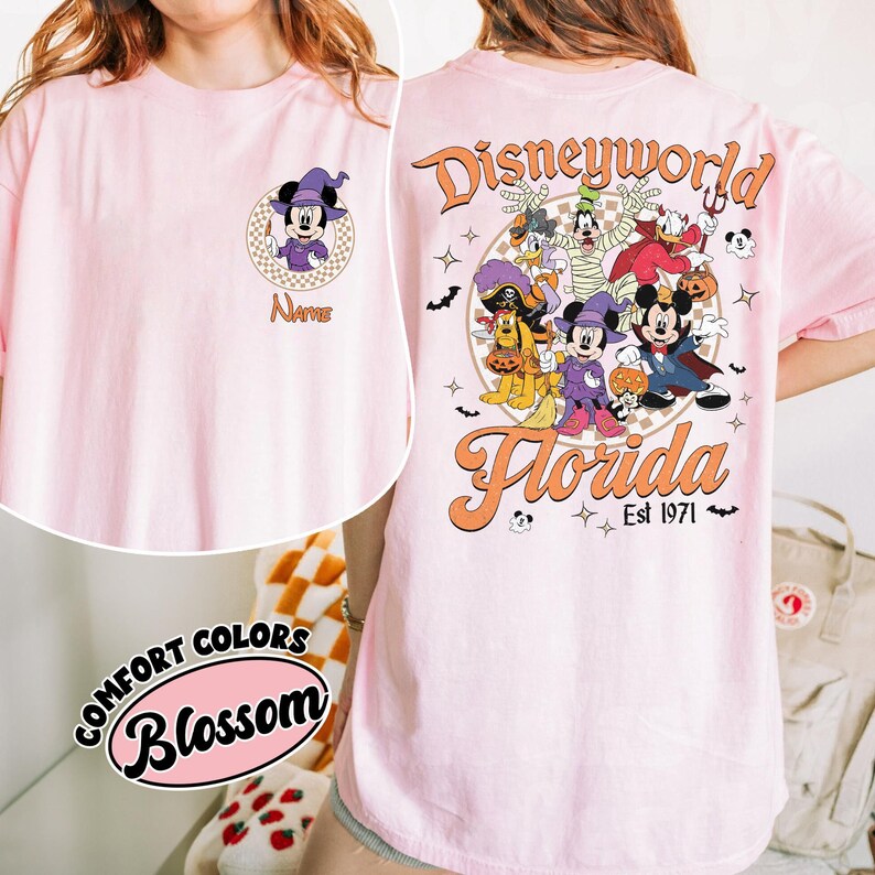 May include: A light pink t-shirt featuring a Halloween-themed Disney World design. The front has a Mickey Mouse graphic with a witch hat and the word "Name". The back displays Disney characters in costumes, with "Disneyworld Florida Est 1971".