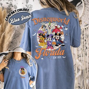 May include: Blue jean t-shirt with a Disney World Florida graphic. The design features various Disney characters in Halloween costumes. The text "Est 1971" is also included in the design. The shirt has the words "Comfort Colors" and "Blue Jean" on the top left.