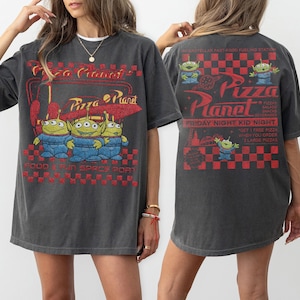 K&ouml;nnte beinhalten: Dunkelgraues T-Shirt mit dem Pizza Planet-Logo und drei gr&uuml;nen Alien-Charakteren. Auf der Vorderseite des Shirts steht "Pizza Planet" und "Food & Fun Space Port". Auf der R&uuml;ckseite des Shirts steht "Friday Night Kid Night".