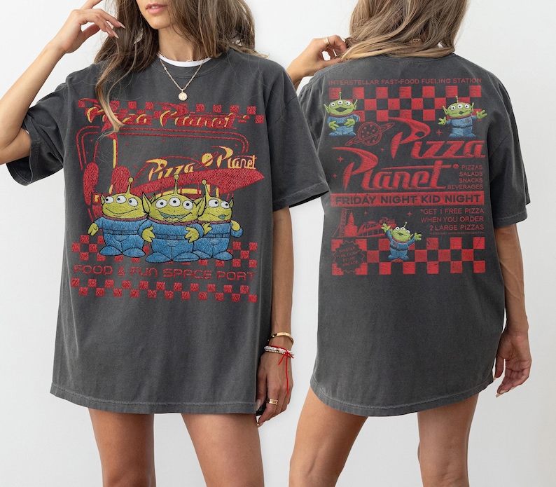 K&ouml;nnte beinhalten: Dunkelgraues T-Shirt mit dem Pizza Planet-Logo und drei gr&uuml;nen Alien-Charakteren. Auf der Vorderseite des Shirts steht "Pizza Planet" und "Food & Fun Space Port". Auf der R&uuml;ckseite des Shirts steht "Friday Night Kid Night".