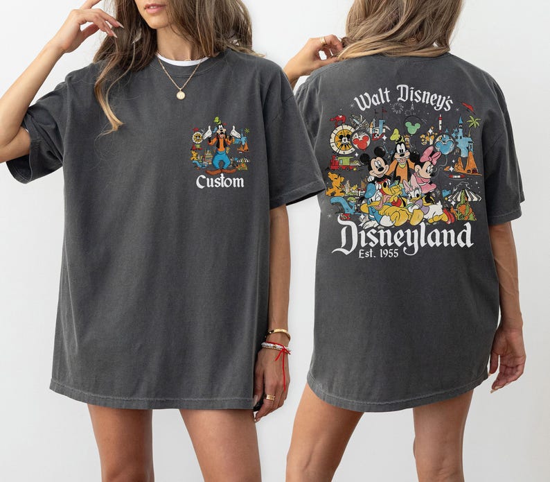 Puede incluir: Camiseta gris oscuro con un gr&aacute;fico de Disneyland en la parte delantera y trasera. El gr&aacute;fico frontal incluye la palabra "Custom". El gr&aacute;fico trasero dice "Walt Disney's Disneyland Est. 1955" con personajes de dibujos animados.