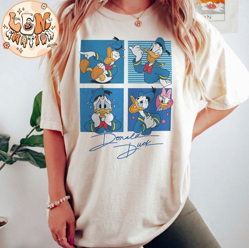 May include: A white t-shirt with a blue and yellow cartoon image of Donald Duck in four different expressions. The text "Donald Duck" is written in black cursive below the image.