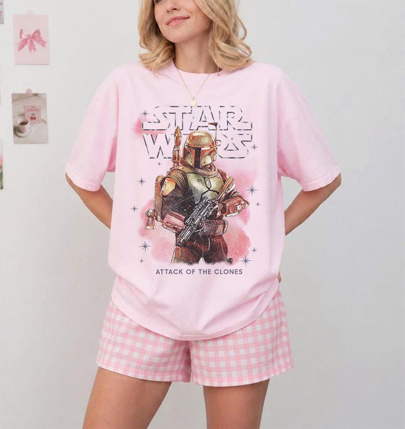 K&ouml;nnte beinhalten: Rosa Star Wars T-Shirt mit Boba Fett Grafik und dem Text "ATTACK OF THE CLONES". Dazu passende rosa-wei&szlig; karierte Shorts. Ein l&auml;ssiges und bequemes Outfit.
