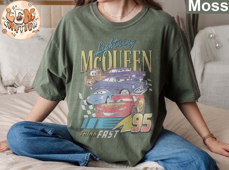 May include: A green t-shirt with a vintage-style graphic of Lightning McQueen from the Cars movie. The graphic features McQueen and other cars from the movie, with the text "Lightning McQueen" and "Think Fast" printed on the shirt.