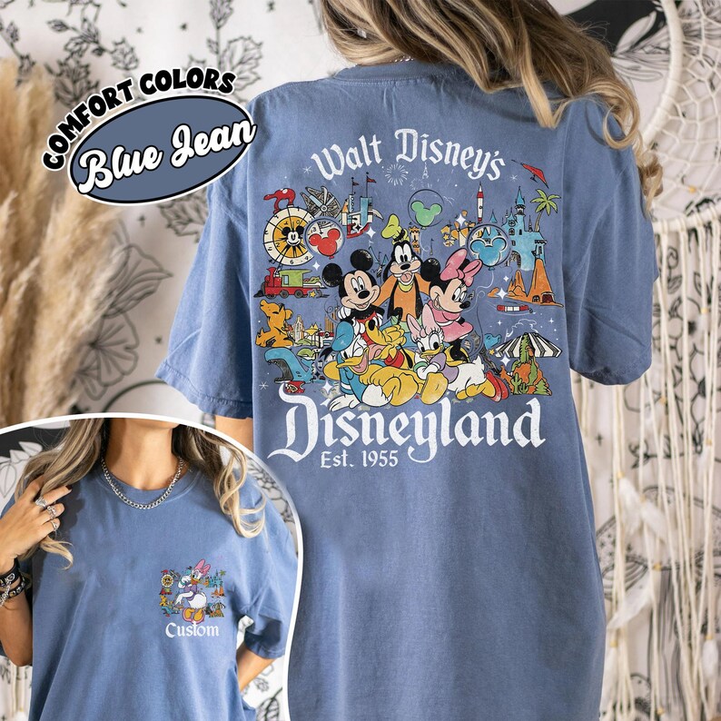 Puede incluir: Camiseta azul vaquero con un gr&aacute;fico de Disneyland en la espalda, con Mickey Mouse, Minnie Mouse y otros personajes de Disney. La parte delantera tiene un gr&aacute;fico m&aacute;s peque&ntilde;o con Daisy Duck y la palabra "Custom". La camiseta tambi&eacute;n tiene las palabras "Comfort Colors" y "Blue Jean".