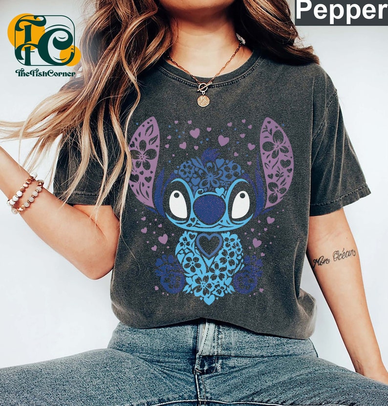 May include: A dark gray t-shirt with a blue and purple Stitch character design. The character is surrounded by hearts and flowers. The text "More Dreams" is visible on the right sleeve.