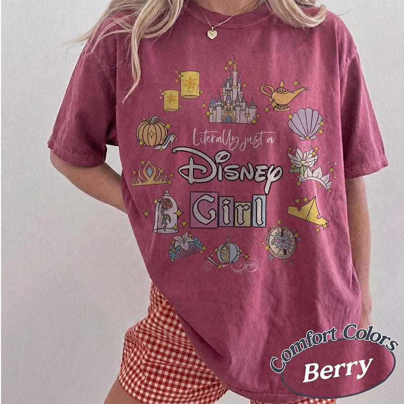 Op de afbeelding: Bessenkleurig T-shirt met de tekst "Literally just a Disney Girl" en diverse Disney-thema graphics. Het shirt heeft een ronde hals en korte mouwen. De woorden "Comfort Colors" en "Berry" staan rechtsonder gedrukt.