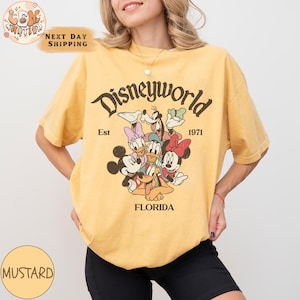 K&ouml;nnte beinhalten: Ein gelbes T-Shirt mit einer Grafik im Vintage-Stil von Mickey Mouse und seinen Freunden. Die Grafik lautet "Disneyworld Est 1971 Florida".