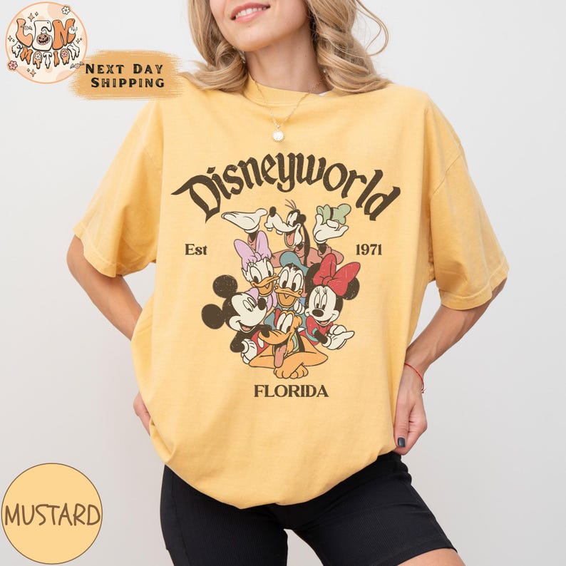 K&ouml;nnte beinhalten: Ein gelbes T-Shirt mit einer Grafik im Vintage-Stil von Mickey Mouse und seinen Freunden. Die Grafik lautet "Disneyworld Est 1971 Florida".