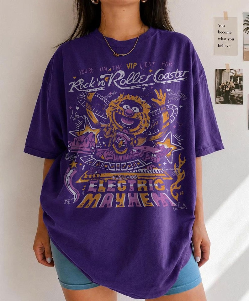 Puede incluir: Camiseta morada con un dise&ntilde;o gr&aacute;fico que incluye el texto "Rock'n Roller Coaster" y "Electric Mayhem", junto con un personaje de dibujos animados y estrellas.