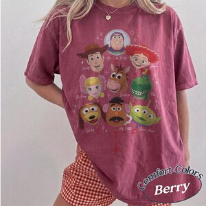 以下が含まれることがあります： ベリー色の半袖Tシャツで、風船の束のように配置されたトイ・ストーリーのキャラクターのグラフィックプリントが施されています。デザインには、ウッディ、バズ・ライトイヤー、ジェシー、ボー・ピープ、ブルズアイ、レックス、スリンキー・ドッグ、ミスター・ポテトヘッド、エイリアンが含まれています。