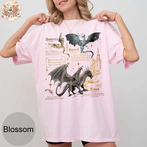 May include: Pink t-shirt with a graphic print of three dragons and their names: Andarna, Sgaevl, and Cairn. The names are written in a gold font.