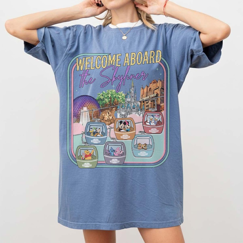 May include: Blue t-shirt with a graphic featuring the text "WELCOME ABOARD The Skyliner" and images of Disney characters in gondolas. The design includes illustrations of various Disney park landmarks.