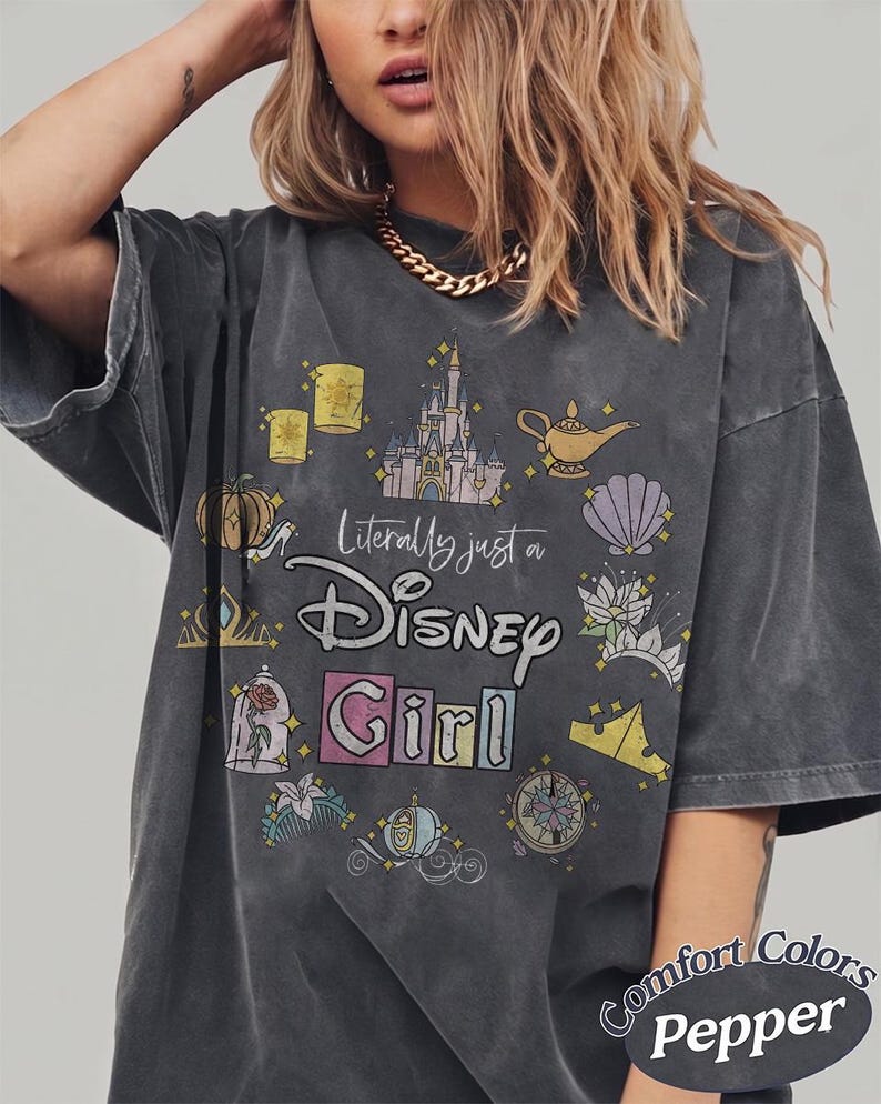 Op de afbeelding: Donkergrijs T-shirt met de tekst "Literally just a Disney Girl" en diverse Disney-thema afbeeldingen. Het shirt heeft een distressed, vintage look en de woorden "Comfort Colors Pepper" staan rechtsonder.