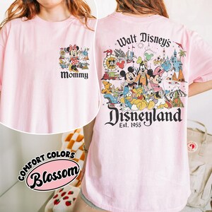 Puede incluir: Camiseta rosa claro con un dise&ntilde;o de Disneyland. La parte delantera presenta un dise&ntilde;o de Minnie Mouse con la palabra "Mommy". La parte trasera muestra una colorida escena de Disneyland con Mickey, Goofy y Donald. La camiseta es Comfort Colors Blossom.