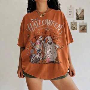 Pu&ograve; includere: T-shirt arancione con grafica da "Nightmare Before Christmas". Il design include personaggi come Jack Skellington, Sally e Oogie Boogie, con la scritta "This is Halloween". La maglietta ha una vestibilit&agrave; ampia.
