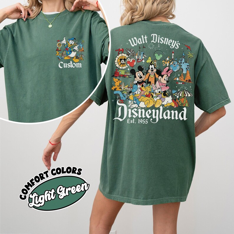 Puede incluir: Camiseta verde claro con tem&aacute;tica de Disney. La parte delantera presenta un gr&aacute;fico de dibujos animados con la palabra "Custom". La parte trasera muestra un gr&aacute;fico colorido de Disneyland con Mickey Mouse, Minnie Mouse y otros personajes. Tambi&eacute;n es visible el texto "Walt Disney's Disneyland Est. 1955".