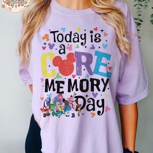 以下が含まれることがあります： カラフルな文字で「Today is a CORE MEMORY Day」と書かれたパープルのTシャツ。テキストはミッキーマウスの耳と星で囲まれています。シャツには、映画「インサイド・ヘッド」のキャラクターも描かれています。