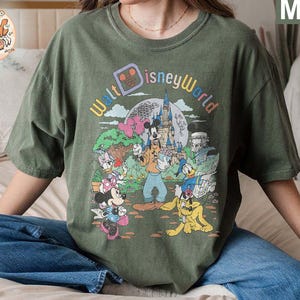May include: A green t-shirt with a vintage-style graphic of Mickey Mouse and friends at Walt Disney World. The text "Walt Disney World" is printed in a colorful arc above the characters.