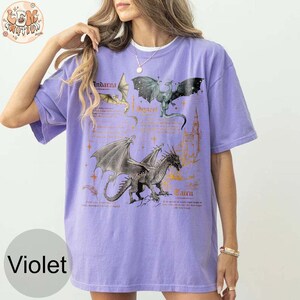 May include: A purple t-shirt with a graphic print of three dragons. The dragons are labeled "Indarva", "Sygra", and "Cairn".