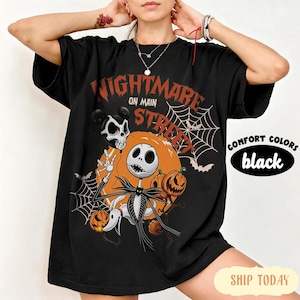 Pu&ograve; includere: Una t-shirt nera con una stampa grafica che riporta il testo Nightmare on Main Street. Il design include un personaggio scheletro, un cane fantasma, zucche, ragnatele e pipistrelli nei colori arancione, bianco e nero. La maglia ha maniche corte.