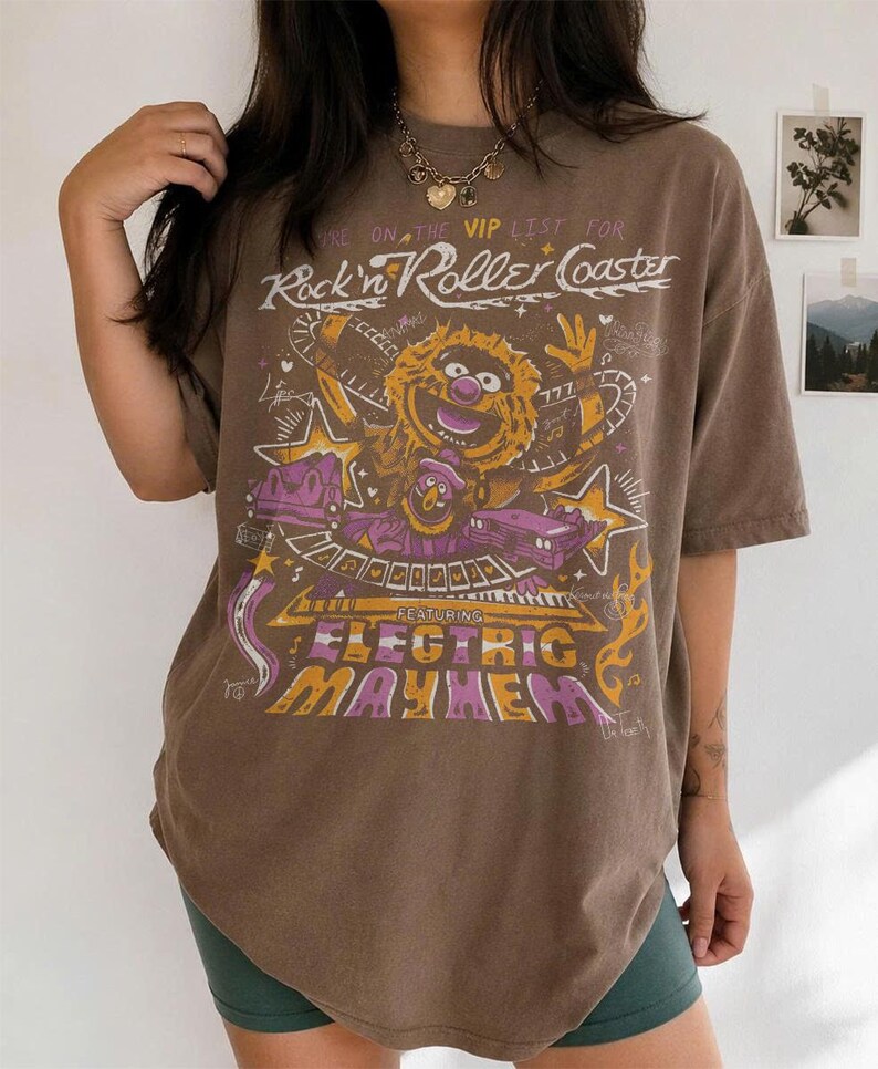 Puede incluir: Camiseta marr&oacute;n con un gr&aacute;fico de un personaje de los Muppets y el texto "Rock'n Roller Coaster" y "Electric Mayhem". La camiseta tiene un aspecto vintage.