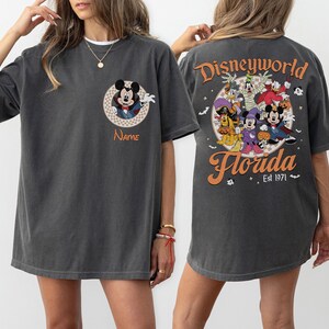 May include: Dark gray t-shirt featuring a Mickey Mouse design on the front and a Disney World Florida graphic on the back. The front design includes a circular Mickey Mouse graphic with the word "Name" below. The back graphic features Disney characters.