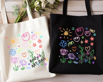 May include: Two tote bags with colorful hand-drawn designs of flowers, hearts, and suns. The text "Andy's Art Bag" is written on each bag. One bag is white and the other is black.