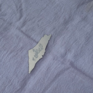 May include: A silver metal outline of the country of Lebanon with the Arabic word "Lebanon" written inside the outline.
