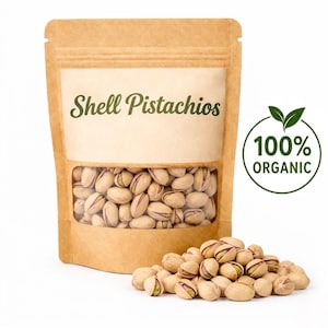 Könnte beinhalten: Ein brauner Papiersack mit einem transparenten Fenster, gefüllt mit Pistazien mit Schale. Der Text "Shell Pistachios" ist auf der Vorderseite aufgedruckt. Ein grüner Kreis mit dem Text "100% ORGANIC" und einem Blattdesign befindet sich auf der rechten Seite. Ein kleiner Haufen Pistazien ist davor.