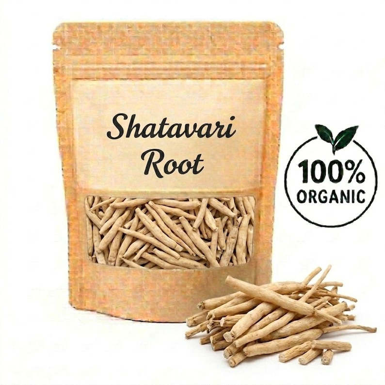 May include: A kraft paper bag with a clear window displaying Shatavari Root. The bag has the text "Shatavari Root" printed on it. A circular label reads "100% ORGANIC". A small pile of Shatavari Root is in front of the bag.