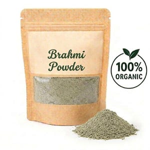 Op de afbeelding: Een bruine papieren zak met Brahmi-poeder met een doorzichtig venster en een hoop poeder ervoor. De tekst "Brahmi Powder" staat op de voorkant. Een cirkelvormig "100% ORGANIC" logo staat rechts.