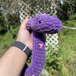 May include: A purple plush snake toy with pink hearts. The snake is curled up and has a fuzzy texture.
