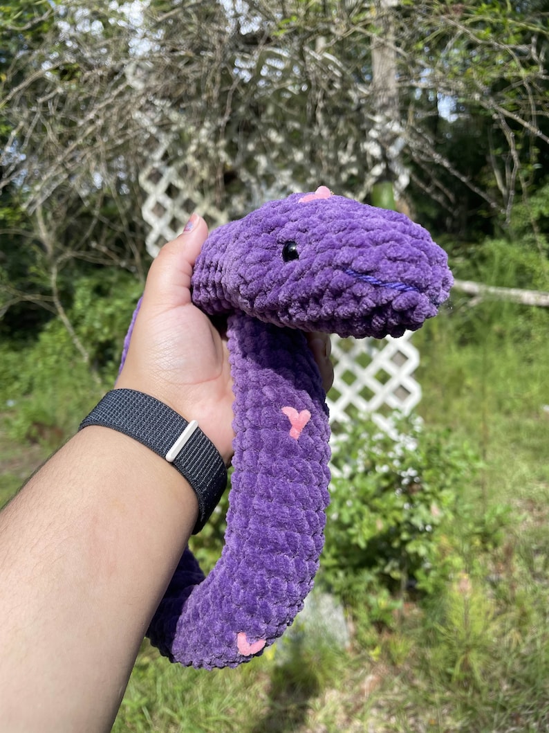 May include: A purple plush snake toy with pink hearts. The snake is curled up and has a fuzzy texture.