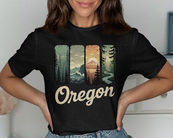 May include: Black t-shirt featuring a vintage-style graphic of Oregon landscapes. The design includes four vertical panels depicting forests, ocean, mountains, and a winding road. The word "Oregon" is written in a cursive font across the bottom.