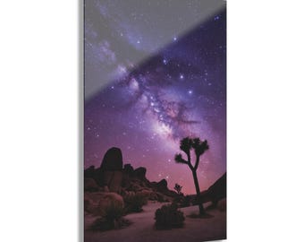May include: A silhouette of a Joshua tree stands in the foreground of a desert landscape under a night sky filled with stars and the Milky Way galaxy. The sky is a vibrant purple and pink.