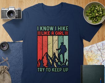 May include: A navy blue t-shirt with a vintage-style graphic featuring a hiker with mountains and the text "I know I hike like a girl try to keep up".